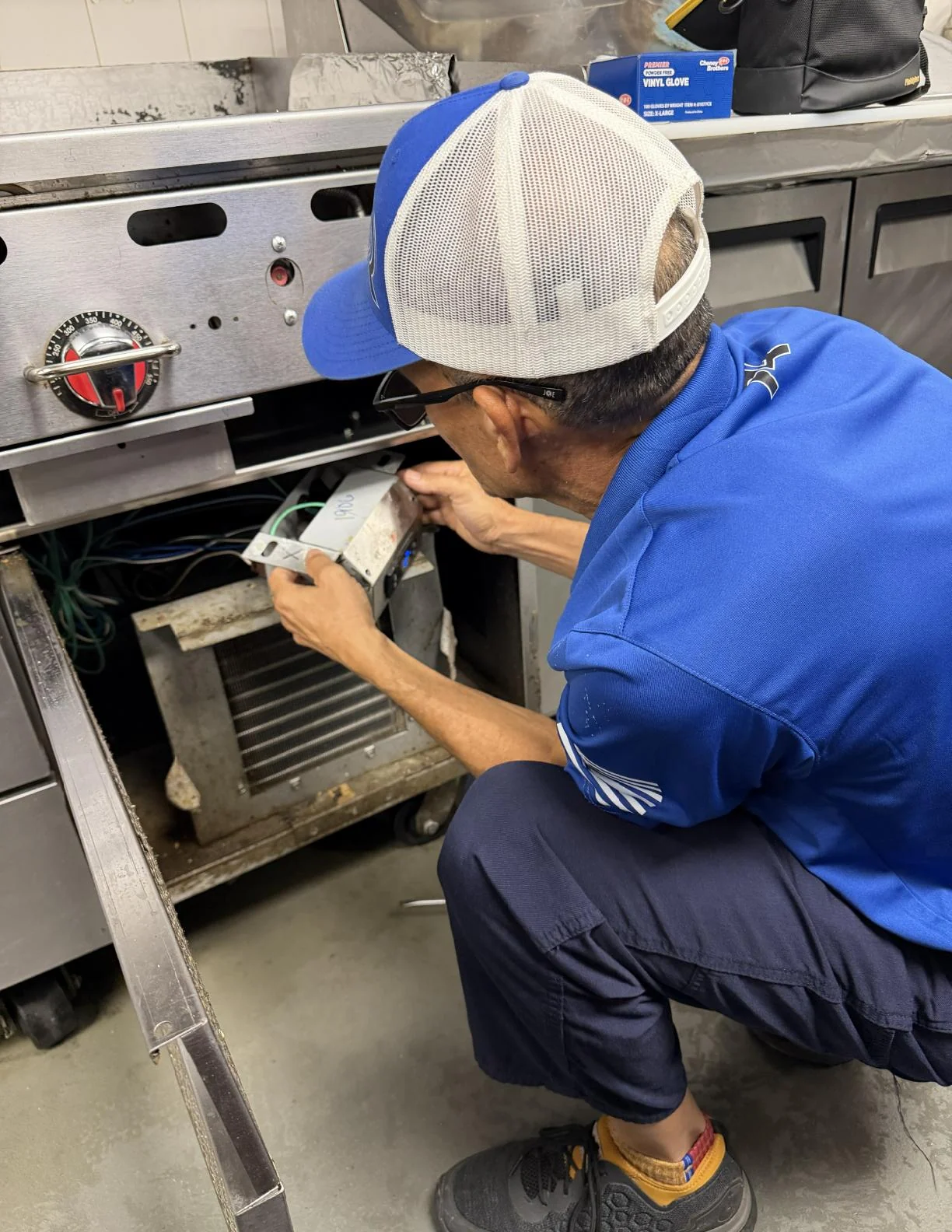 2R Cooling technician working at the controls of a commercial undercounter cooler in a West Palm Beach restaurant kitchen