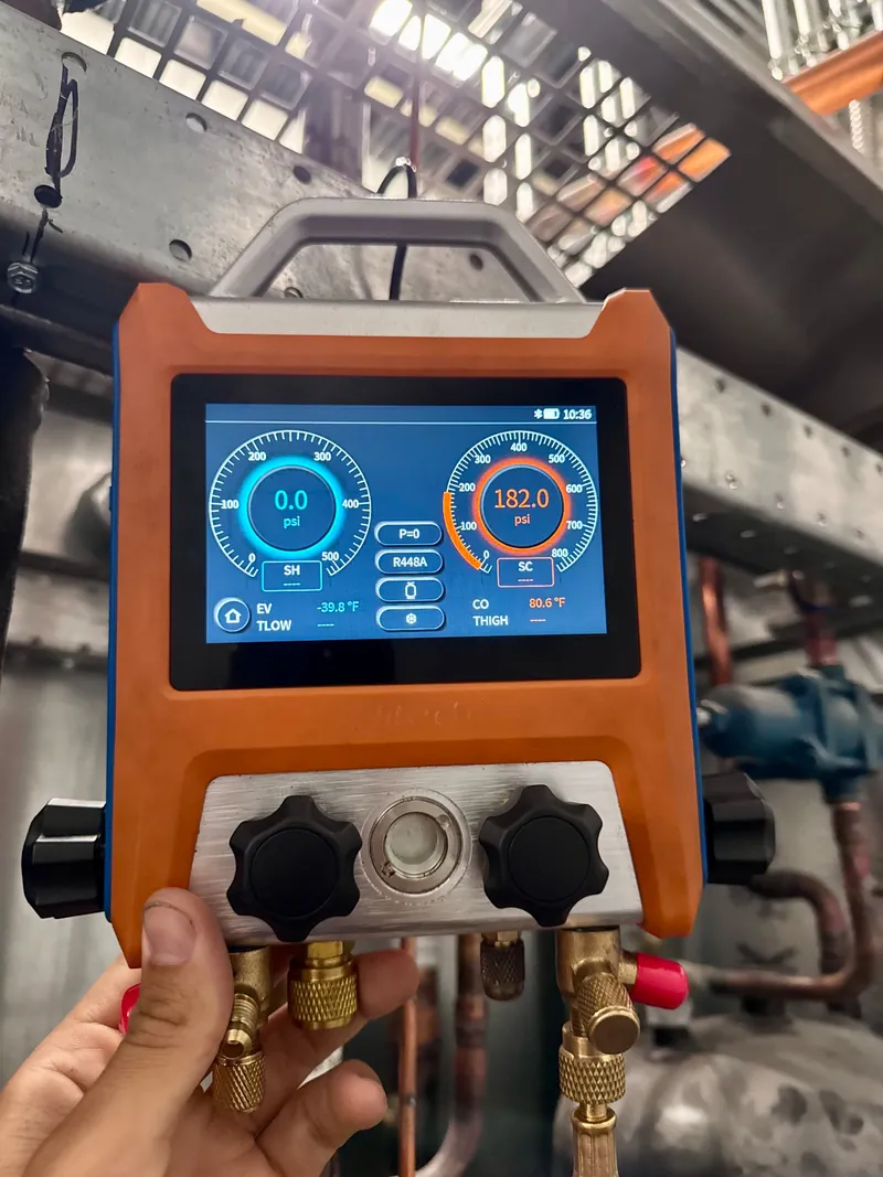 Technician holding electronic refrigerant gauges displaying 0 psi and 182 psi at the supermarket rack