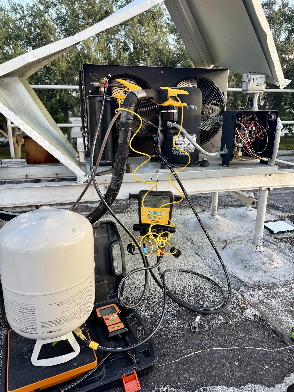 Walk-in freezer condensing unit on a West Palm Beach rooftop with a Fieldpiece digital manifold, temperature probes and a refrigerant cylinder on a charging scale