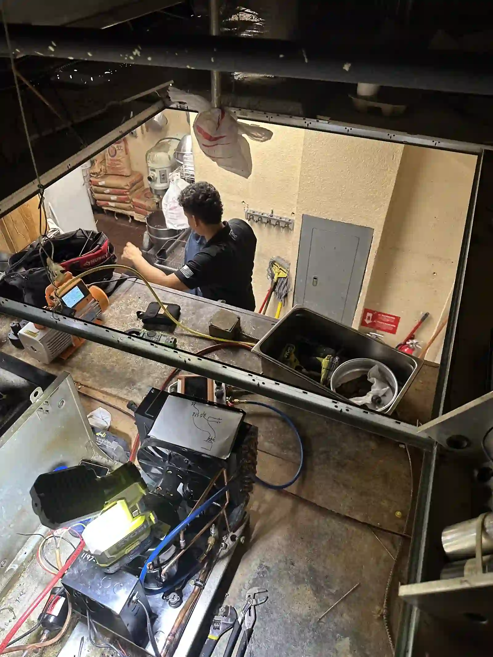 Overhead view of a 2R Cooling technician servicing the walk-in cooler refrigeration system at Alfonso's Pizza in Port St. Lucie, with gauges and recovery equipment staged below the unit