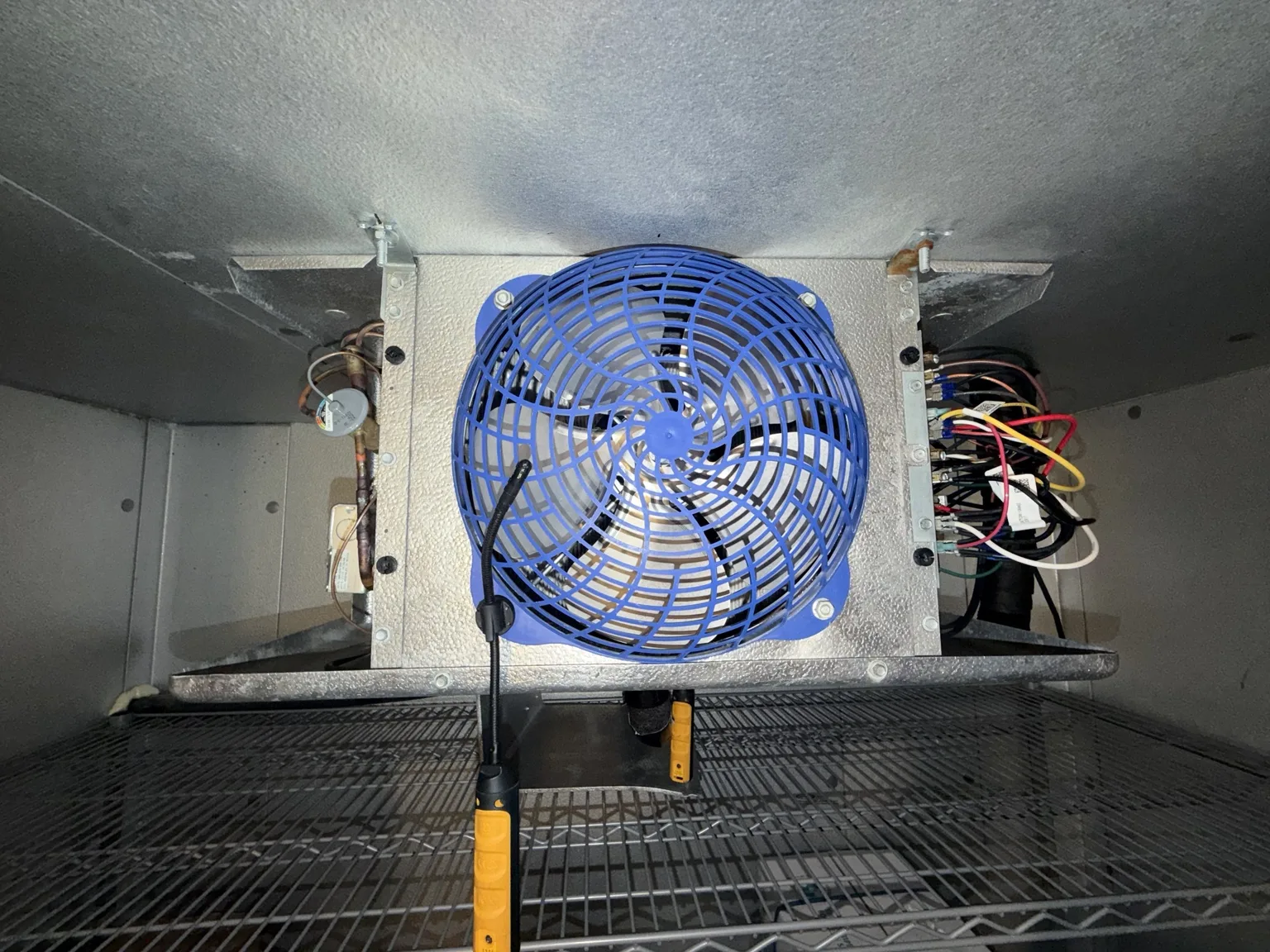 Walk-in freezer evaporator with blue fan guard and a Fieldpiece temperature probe during testing